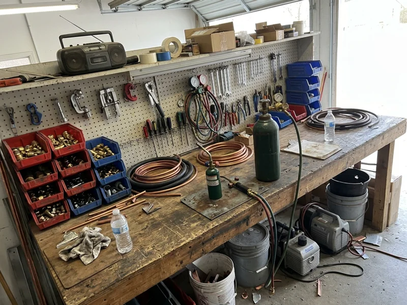 Shop workbench with copper line sets, brazing gear and labelled heat pump parts bins