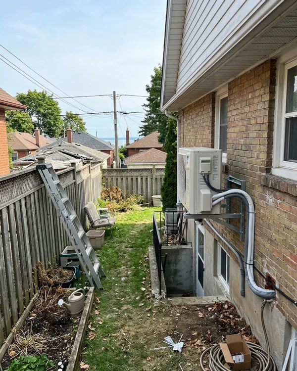 Air-source heat pump on a sheltered bracket behind the Mimico bungalow