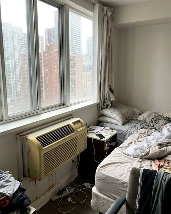 Old yellowed PTAC unit under a window in a condo bedroom