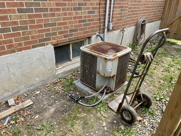 Old builder-grade heat pump disconnected and ready for removal