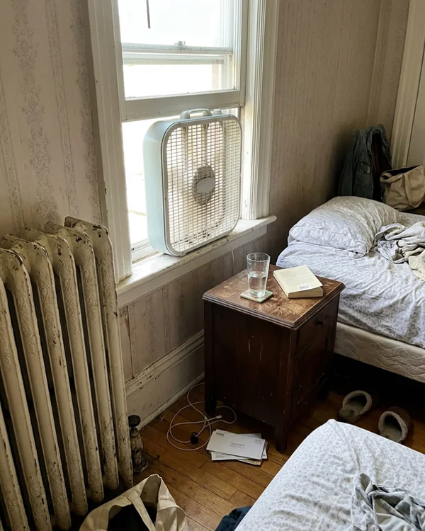 Radiator and window fan in a Victorian bedroom before the heat pump