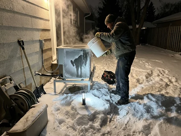 Technician de-icing an outdoor coil in deep snow